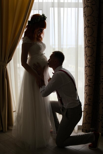 Photo le marié embrasse le ventre de la mariée enceinte longueur complète silhouette sombre