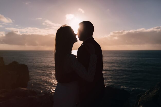 Le marié étreint la jeune mariée sur le rivage rocheux et les rayons du