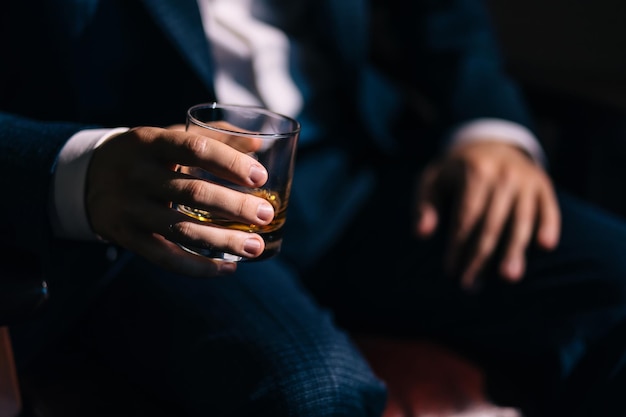Le marié l'homme d'affaires est assis et tient un verre de whisky Préparer le marié pour le matin du mariage Gros plan