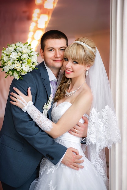 Le marié et la mariée avec un bouquet de mariage se tiennent près d'une colonne blanche