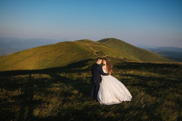 Marié et mariée sur la colline dans les montagnes. Couple de mariage en face de la colline verte.