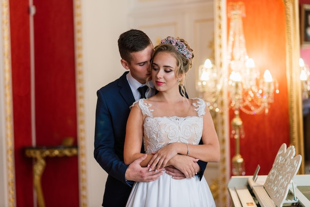Le marié et la mariée étreignant et embrassant près du piano dans un intérieur de luxe