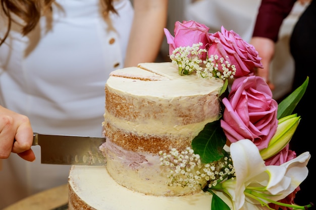 Marié et mariée en robe blanche coupe couche gâteau de mariage nu, décoré de fleurs fraîches