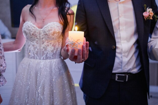 Le marié et la mariée tiennent une bougie dans leurs mains