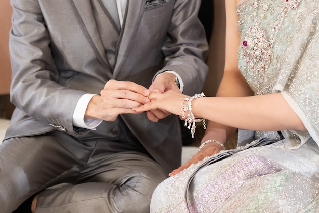 Le marié met une bague de mariage dans un doigt de la mariée inThai Wedding Concept