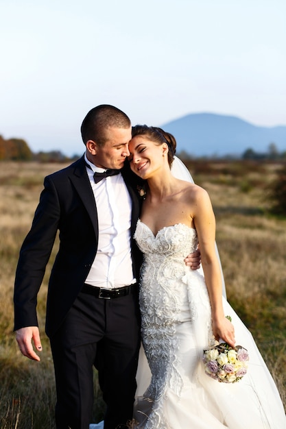 Le marié regarde la mariée impressionnante tenant sa taille pendant qu&#39;ils marchent à travers le champ