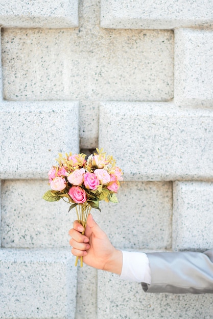 Marié tenant un bouquet de fleurs roses roses et fond de mur en béton.