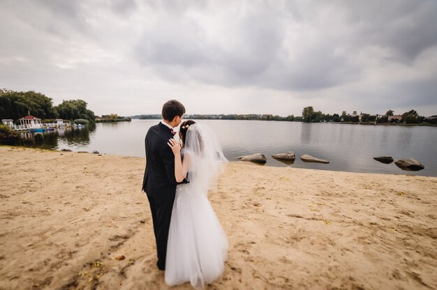 Le marié tient la mariée sur le sable près du lac.