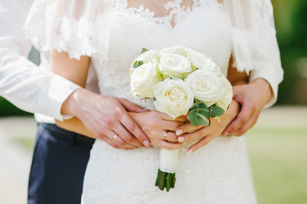 Le marié tient ses mains sur celui de la mariée pendant qu&#39;elle tient le bouquet de mariage des roses blanches