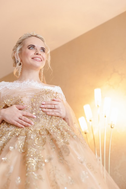 Mariée blonde souriante dans une robe beige chic dans une chambre d'hôtel