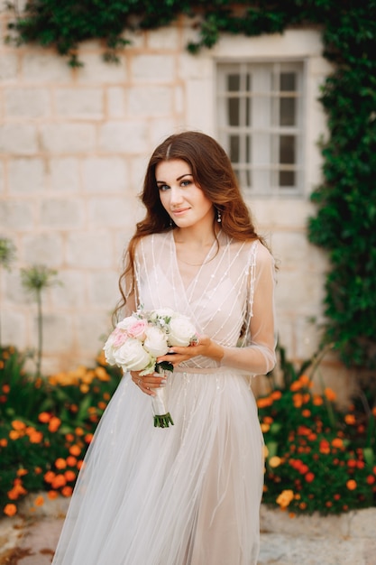 Une mariée avec un bouquet dans ses mains se tient au mur d'une maison avec une liane verte et orange