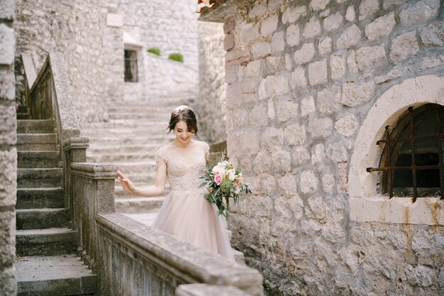 La mariée avec un bouquet descend les marches d'un bâtiment en pierre