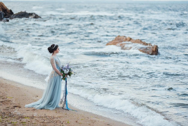 Mariée avec un bouquet de fleurs sur la plage près de l'eau