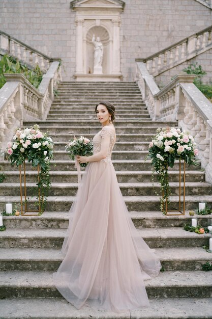 Mariée avec un bouquet sur les marches en pierre d'une ancienne villa