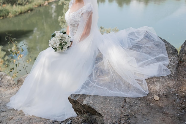 Mariée avec un bouquet sur les pierres près du lac