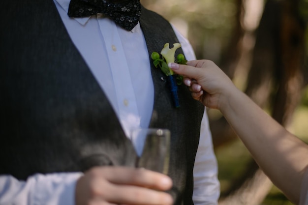 La mariée corrige la boutonnière du marié lors de leur mariage. Détails en gros plan. coup d'une mariée. mise au point douce