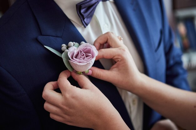 La mariée corrige la boutonnière du marié sur la veste lors de leur mariage