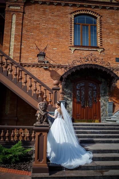 Mariée dans une belle robe blanche et longue sur fond d'un immeuble en brique