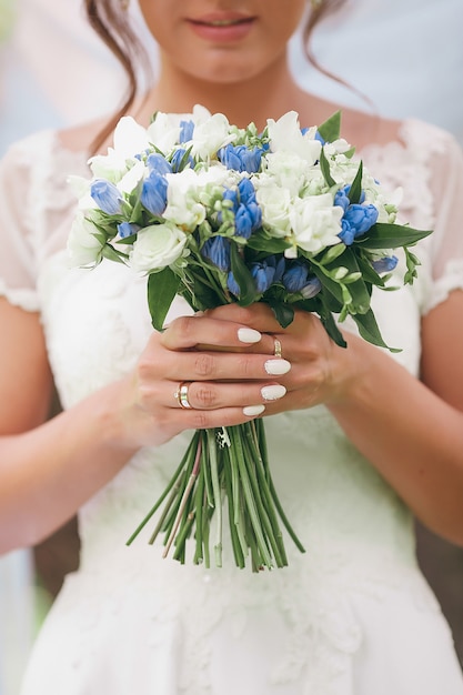 Une mariée dans une belle robe avec un train tenant un bouquet de fleurs et de verdure