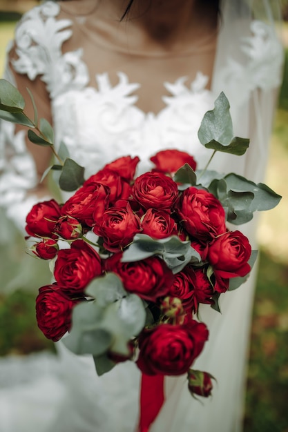 Une mariée dans une belle robe avec un train tenant un bouquet de fleurs et de verdure