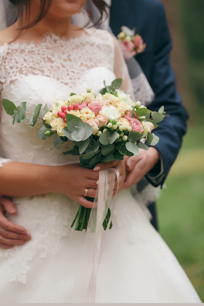 Une mariée dans une belle robe avec un train tenant un bouquet de fleurs et de verdure