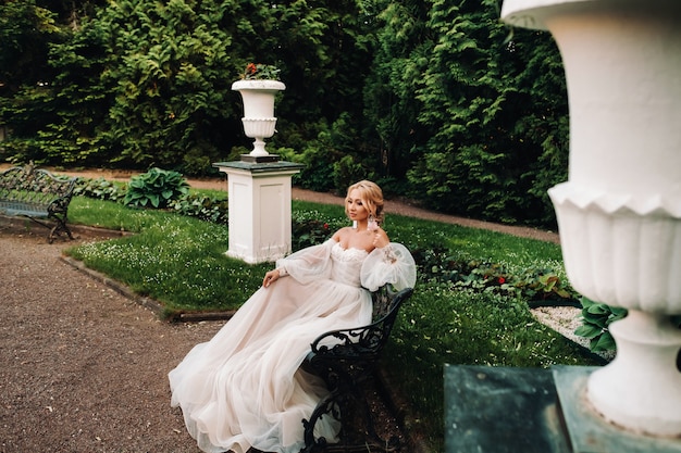 Mariée dans le jardin, mariée assise sur un banc, mariée rassemblant, mariée du matin, robe blanche, mettre des boucles d'oreilles.
