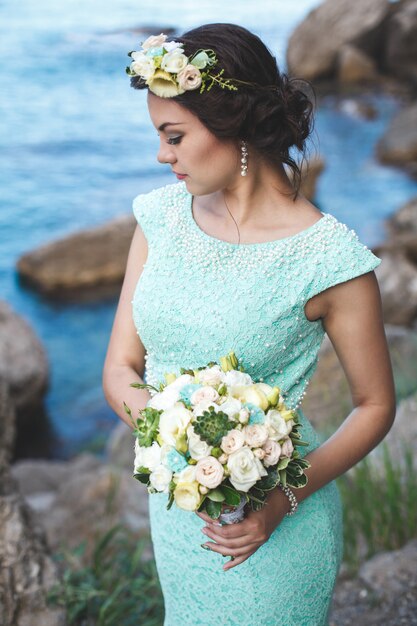 Mariée dans la nature dans les montagnes près de l'eau. Robe couleur Tiffany. Mariée posant avec bouquet.