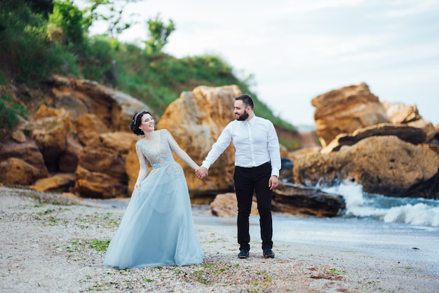 mariée dans une robe bleue marche le long du rivage de l'océan