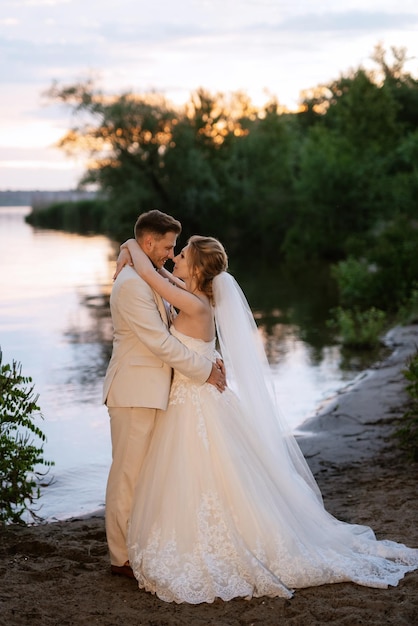 Mariée dans une robe bouffante blanche et le marié en t sur la rive du fleuve