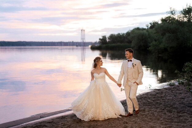 Mariée dans une robe bouffante blanche et le marié en t sur la rive du fleuve