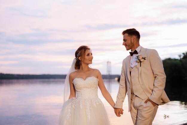 Mariée dans une robe bouffante blanche et le marié en t sur la rive du fleuve