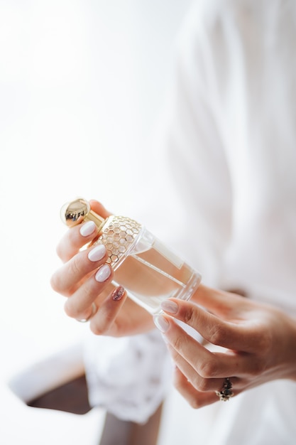 Mariée dans une robe en dentelle blanche tient une bouteille de parfum