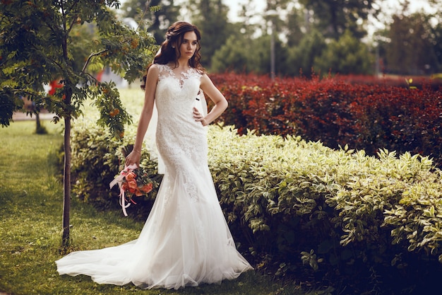 La mariée dans une robe de mariée blanche se dresse dans le contexte d'une cascade artificielle dans un parc de la ville