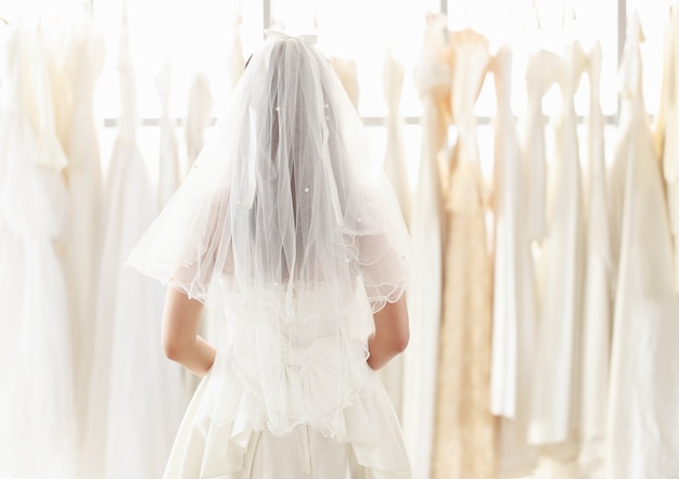 La mariée dans une robe de mariée en dentelle blanche se tient en arrière et regarde la robe de mariée dans la cabine d'essayage. Femme choisissant de nombreuses robes de mariée dans la boutique.