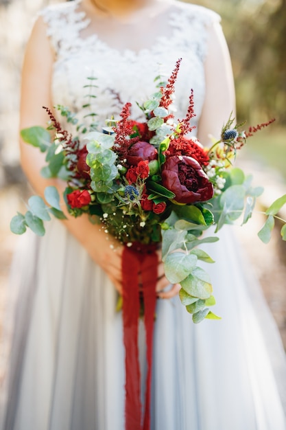 Une mariée dans une robe de mariée gris pâle est titulaire d'un bouquet de pivoines rouges Astilba roses et érythème et