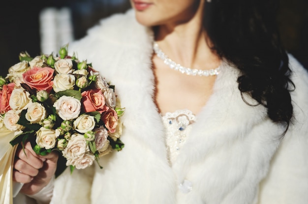 Mariée dans une robe de mariée et un manteau blanc tenant un beau nous