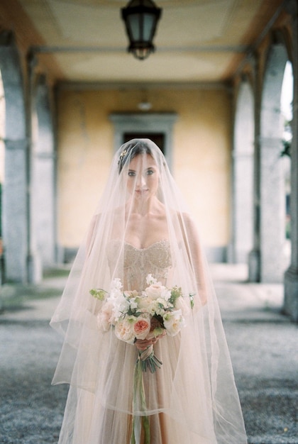 La mariée dans un voile avec un bouquet se tient sur une terrasse avec des colonnes Côme Italie