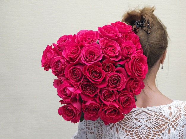 La mariée debout en arrière tenant un grand bouquet de roses sur son épaule.