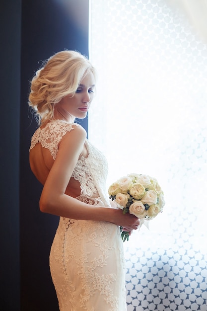 Mariée du matin. Une femme en robe de mariée blanche tenant un bouquet de fleurs dans ses mains. Belle fille blonde se prépare pour la cérémonie de mariage