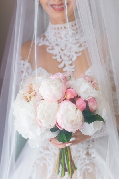 Mariée élégante dans une belle robe tient un bouquet de mariée et recouverte de voile