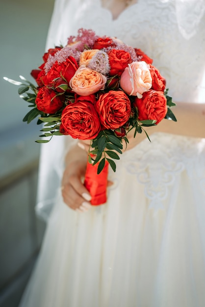 Mariée élégante dans une robe blanche détient un gros plan de bouquet de mariage lumineux. Bouquet de mariée de fleurs rouges dans les mains d'une jeune mariée.