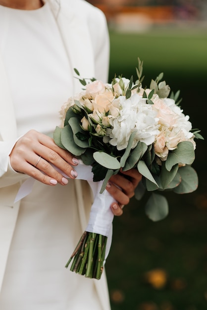 Mariée élégante dans une robe blanche et manucure tenant un bouquet de mariage