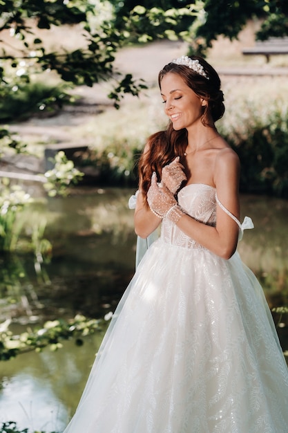 Une mariée élégante en robe blanche, des gants avec un bouquet sur une cascade dans le parc, profitant de la nature.Modèle en robe de mariée et gants dans la forêt.Biélorussie