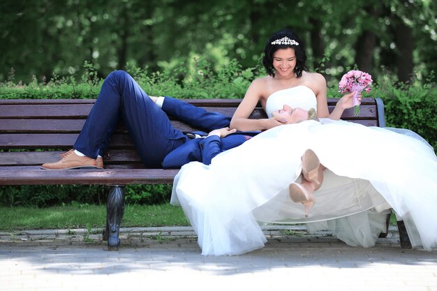 La mariée embrasse le marié, assise sur un banc de parc par une journée ensoleillée.