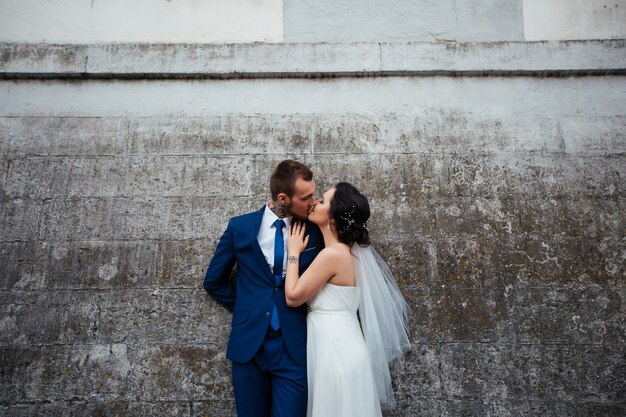 La mariée embrasse son fiancé sur un fond de mur gris