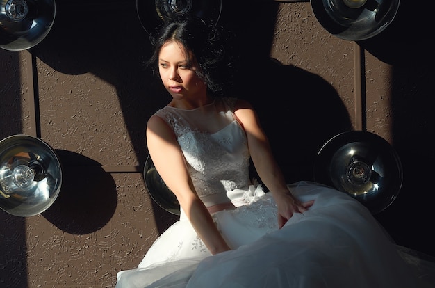 La mariée est assise sur le canapé et regarde par la fenêtre robe de mariée sun ray