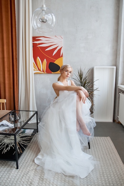 Mariée femme dans une robe de mariée d'été légère assise à la fenêtre et en attente de la cérémonie de mariage