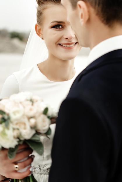 Mariée heureuse à la recherche d'un marié élégant sur la côte sablonneuse et mariage de luxe souriant