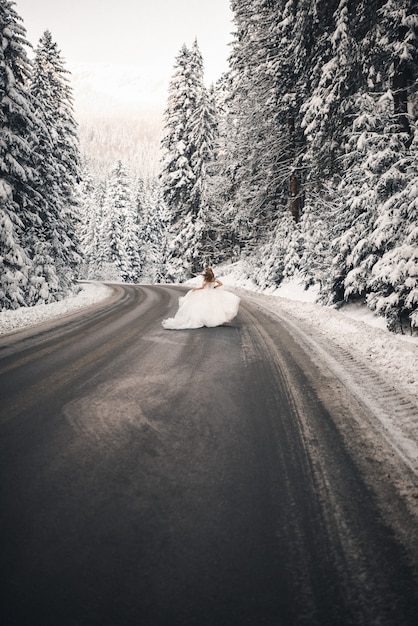 La mariée longe la route près des arbres enneigés