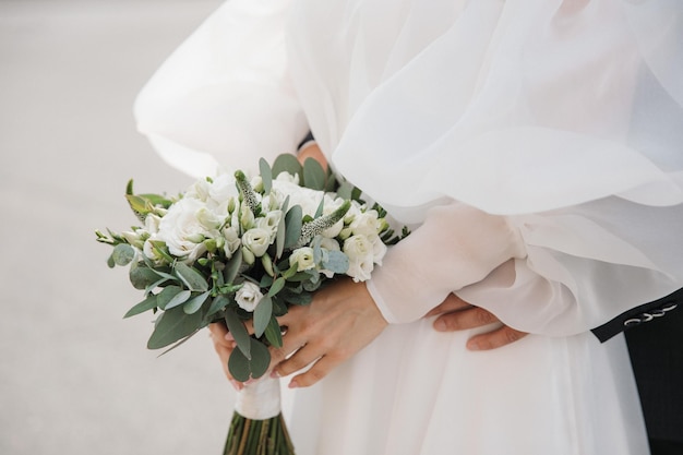 Une mariée avec des manches tient un bouquet de mariée devant elle